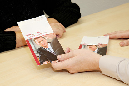 Hände einer Person, die einer anderen den Flyer „Anwaltliche Beratungsstellen“ reicht