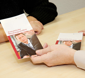Hände einer Person, die einer anderen den Flyer „Anwaltliche Beratungsstellen“ reicht