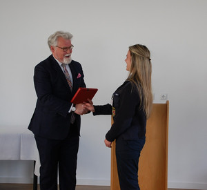 Justizminister Herbert Mertin überreicht der Lehrgangsbasten Celine Quint eine Urkunde und schüttelt ihre Hand
